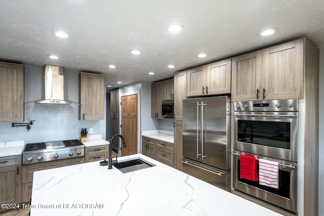 kitchen featuring light stone countertops, appliances with stainless steel finishes, sink, and wall chimney exhaust hood