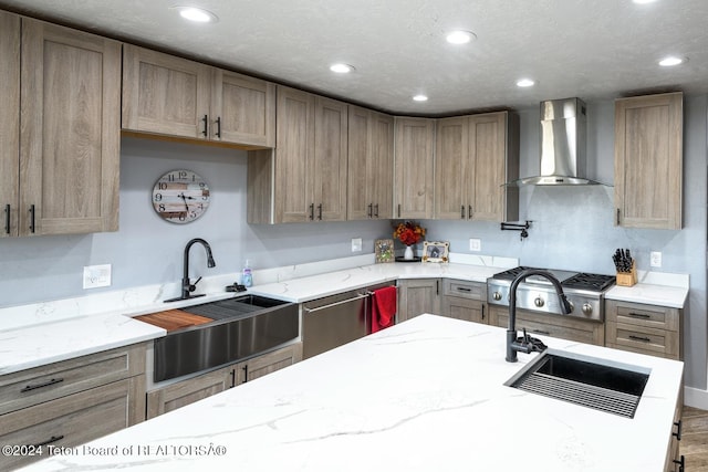 kitchen with wall chimney range hood, stainless steel appliances, sink, and light stone countertops