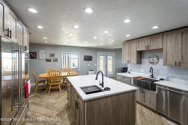 kitchen featuring french doors, stainless steel appliances, sink, and an island with sink