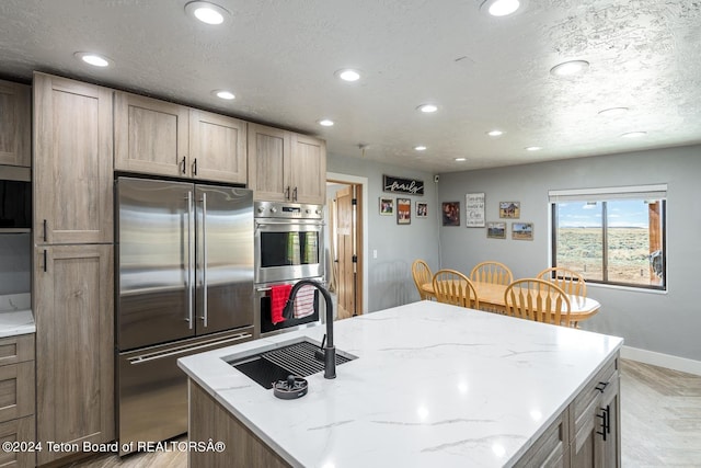 kitchen with sink, stainless steel appliances, a center island, light stone counters, and light parquet flooring