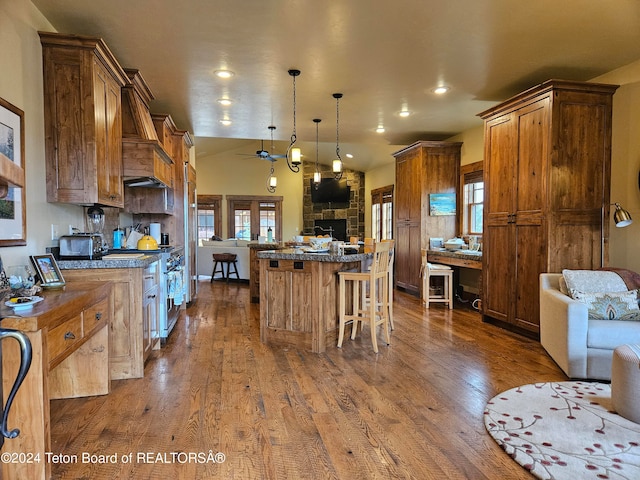 kitchen featuring a breakfast bar, dark wood-type flooring, ceiling fan, a fireplace, and a center island with sink