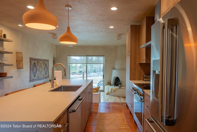 kitchen with hanging light fixtures, premium appliances, a center island with sink, a fireplace, and sink