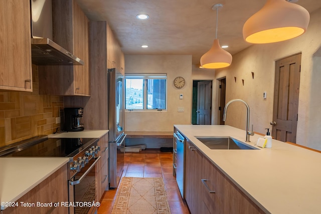 kitchen with decorative light fixtures, premium appliances, wall chimney range hood, tasteful backsplash, and sink