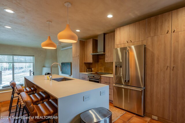 kitchen with sink, a kitchen bar, wall chimney range hood, high quality appliances, and pendant lighting