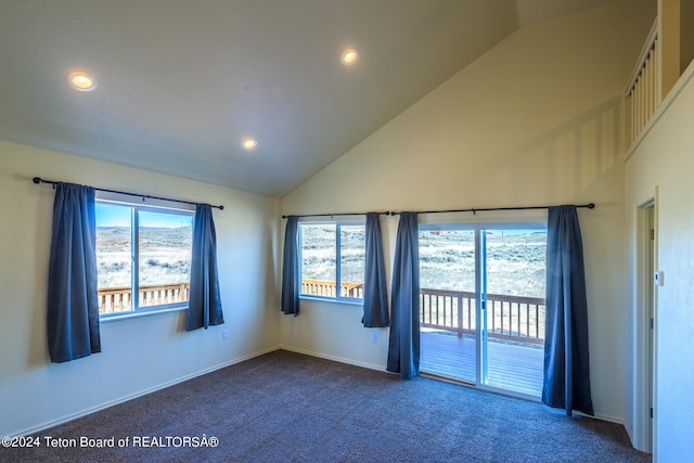 spare room with dark colored carpet, plenty of natural light, and high vaulted ceiling