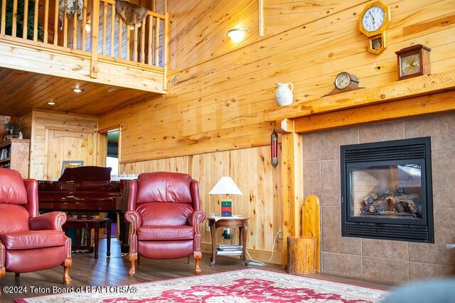 living room with wood-type flooring, wooden walls, and a tiled fireplace