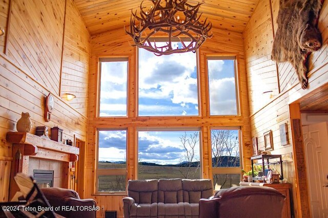 living room featuring high vaulted ceiling, wood walls, and an inviting chandelier