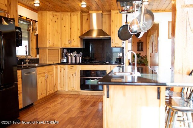 kitchen featuring light hardwood / wood-style floors, wooden ceiling, black appliances, wall chimney exhaust hood, and sink