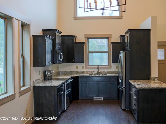 kitchen with a chandelier, stainless steel appliances, dark hardwood / wood-style flooring, sink, and light stone countertops