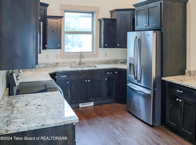 kitchen with sink, light stone counters, stove, dark hardwood / wood-style floors, and stainless steel fridge