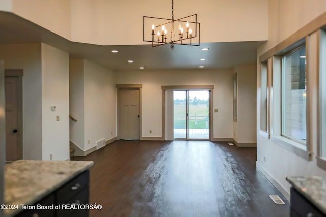 unfurnished dining area with an inviting chandelier, dark hardwood / wood-style floors, and a towering ceiling