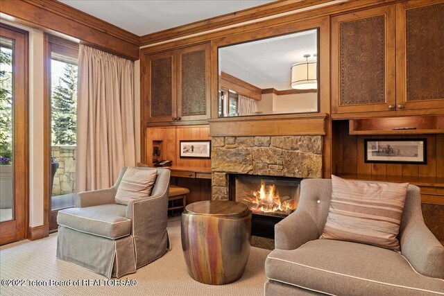 sitting room with a stone fireplace, light carpet, ornamental molding, and wood walls