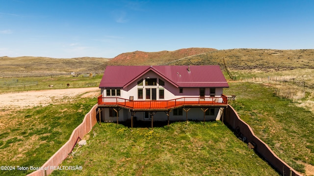 rear view of property featuring a yard, a deck with mountain view, and a rural view