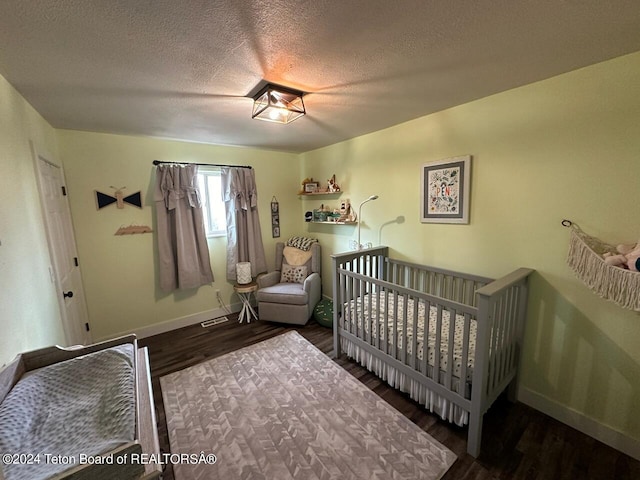 bedroom with dark wood-type flooring, a textured ceiling, and a nursery area