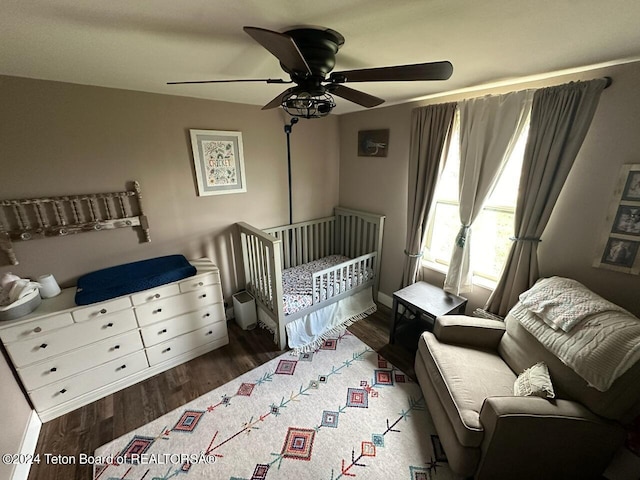 bedroom featuring ceiling fan, dark hardwood / wood-style floors, and a nursery area