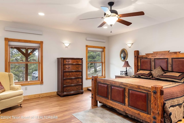 bedroom with ceiling fan, a wall mounted AC, and light hardwood / wood-style flooring