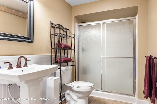 bathroom with toilet, a shower with door, and sink