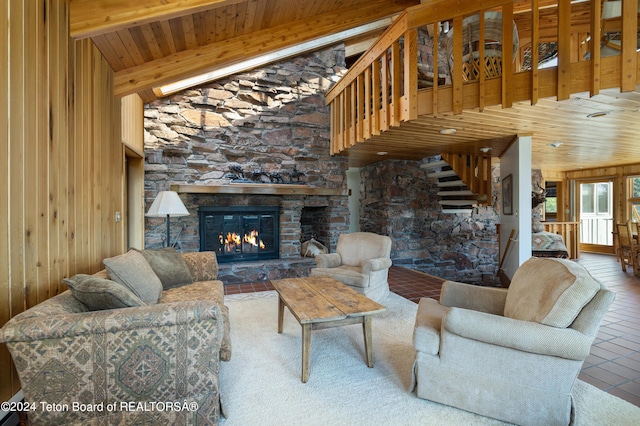 living room featuring wood walls, a stone fireplace, and high vaulted ceiling