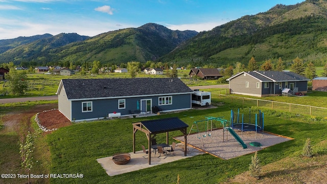 rear view of house with an outdoor fire pit, a playground, a patio area, and a mountain view