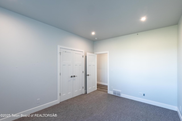 unfurnished bedroom with dark carpet and a closet