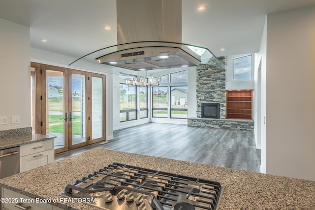 kitchen featuring gas stovetop, white cabinetry, island exhaust hood, a fireplace, and light stone countertops