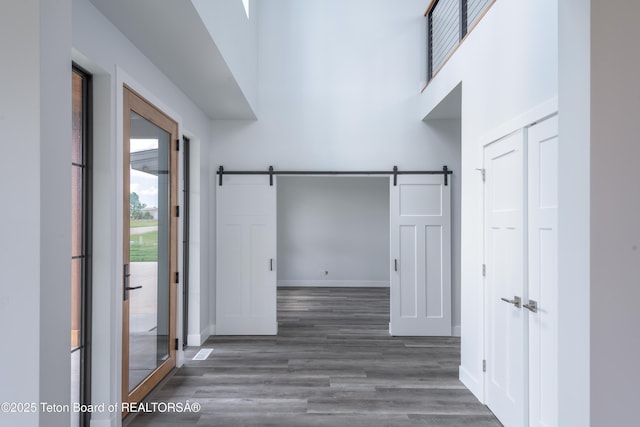 hallway with a high ceiling, a barn door, and dark hardwood / wood-style flooring