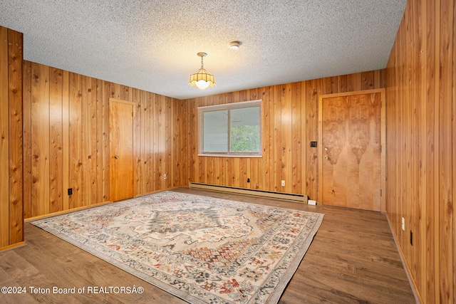 unfurnished room featuring baseboard heating, a textured ceiling, wood-type flooring, and wood walls