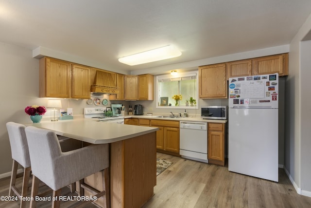 kitchen featuring kitchen peninsula, light wood-type flooring, a breakfast bar, custom range hood, and white appliances