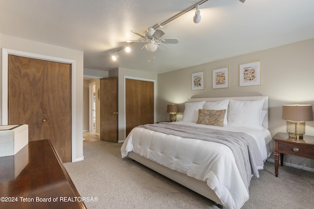 carpeted bedroom with a textured ceiling, rail lighting, ceiling fan, and multiple closets