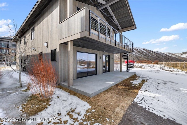 view of snowy exterior with a patio area, a mountain view, and stairway