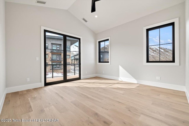 spare room with vaulted ceiling, plenty of natural light, baseboards, and light wood-style floors