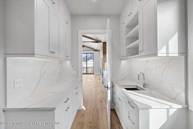 kitchen with a sink, backsplash, light wood finished floors, and light stone countertops