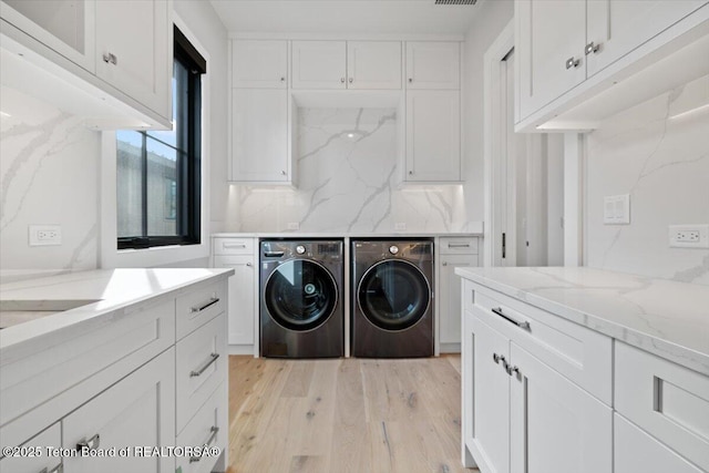 washroom featuring cabinet space, visible vents, light wood-style floors, and washing machine and clothes dryer