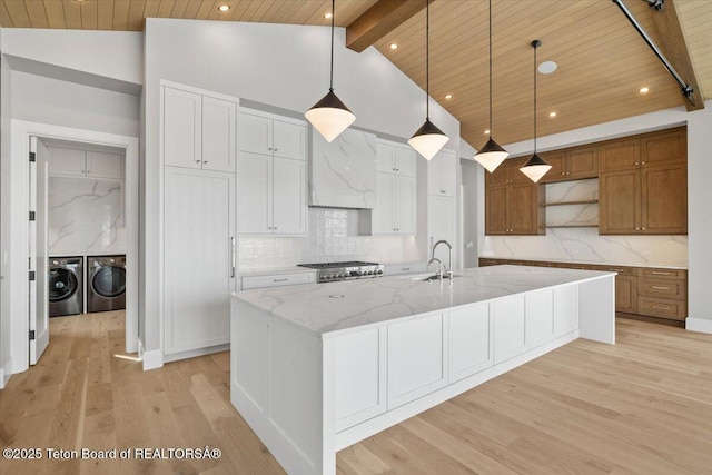 kitchen with open shelves, stove, light wood-style floors, washing machine and dryer, and wall chimney range hood