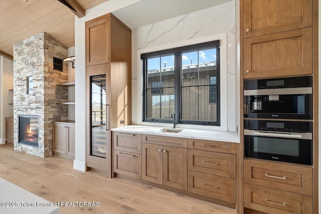 kitchen featuring light wood-style flooring, brown cabinets, multiple ovens, light countertops, and a fireplace