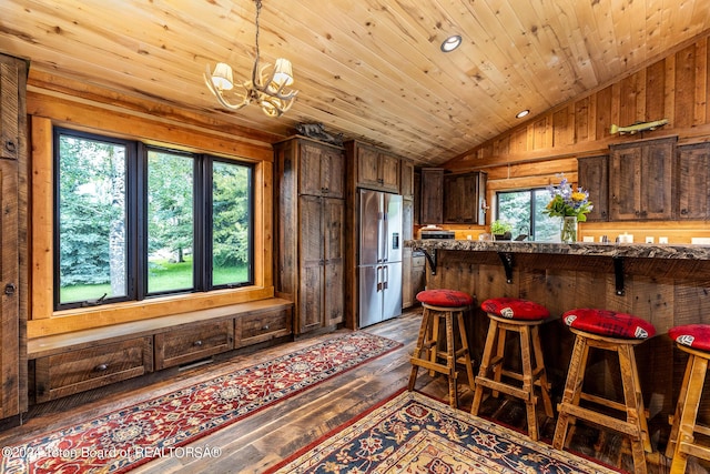 kitchen featuring high quality fridge, lofted ceiling, a kitchen bar, a notable chandelier, and wood ceiling