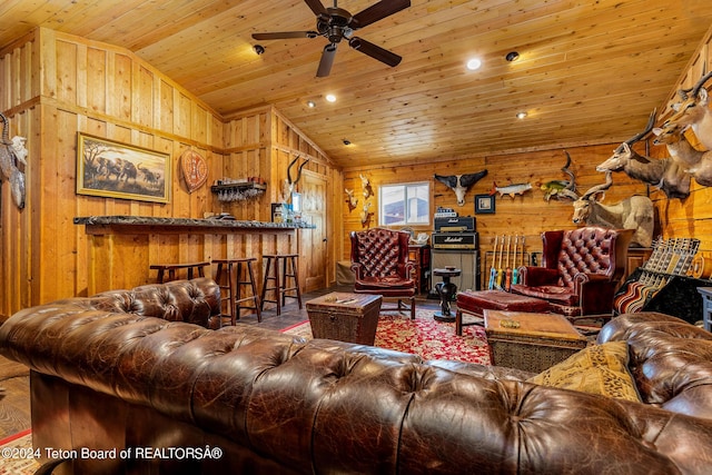 living room featuring vaulted ceiling, wooden walls, wooden ceiling, ceiling fan, and bar area