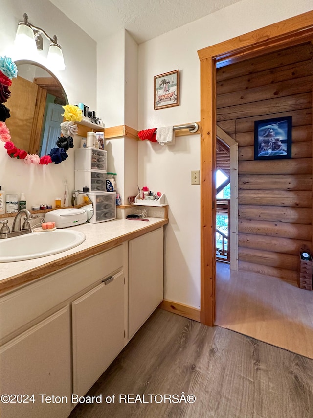 bathroom with vanity, a textured ceiling, hardwood / wood-style floors, and rustic walls