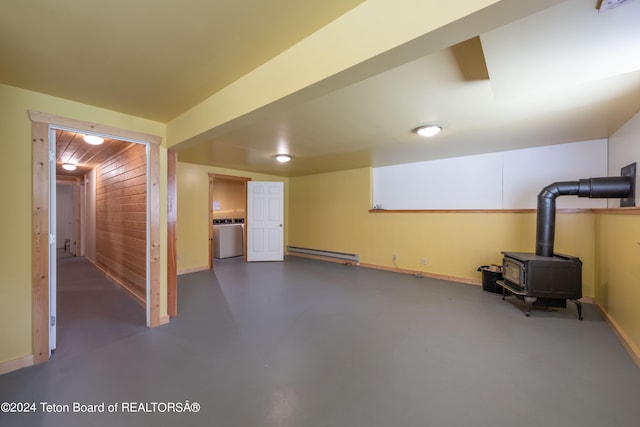 finished below grade area featuring baseboard heating, a wood stove, wooden walls, washer / dryer, and baseboards