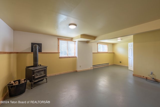 below grade area with a baseboard heating unit, a wood stove, and baseboards