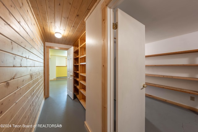 corridor with a baseboard heating unit, wood walls, wooden ceiling, and concrete flooring