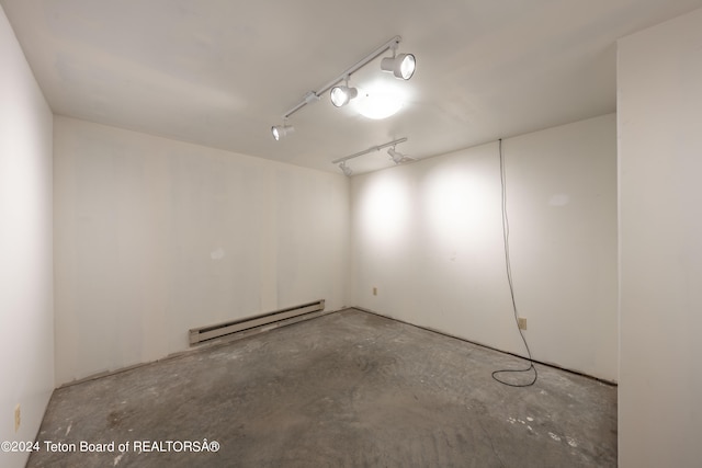 empty room featuring track lighting, a baseboard radiator, and unfinished concrete floors