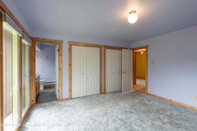 unfurnished bedroom featuring ensuite bathroom, a baseboard radiator, baseboards, multiple closets, and carpet