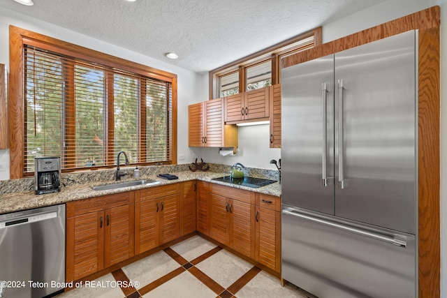 kitchen featuring stainless steel appliances, sink, a textured ceiling, and light stone counters