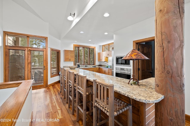 kitchen with sink, light stone countertops, built in microwave, oven, and light wood-type flooring