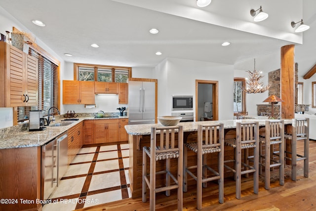 kitchen with a breakfast bar, sink, light stone counters, black appliances, and an inviting chandelier