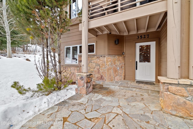 snow covered property entrance featuring a balcony