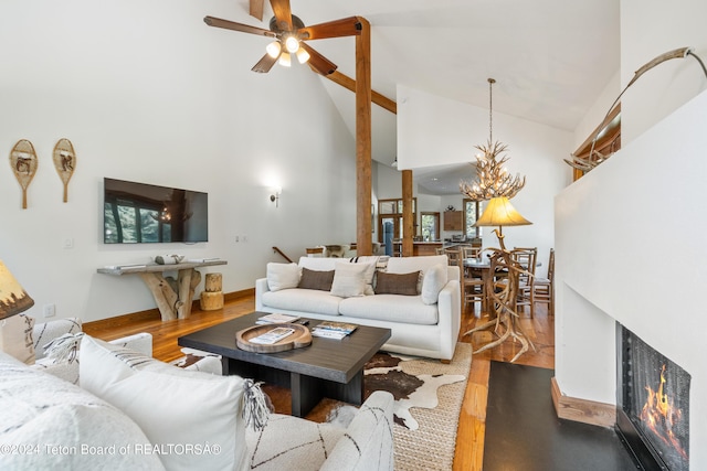 living room featuring high vaulted ceiling, ceiling fan with notable chandelier, and wood-type flooring