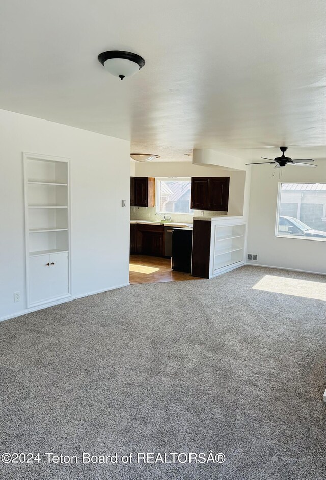 unfurnished living room with sink, carpet floors, a healthy amount of sunlight, and ceiling fan