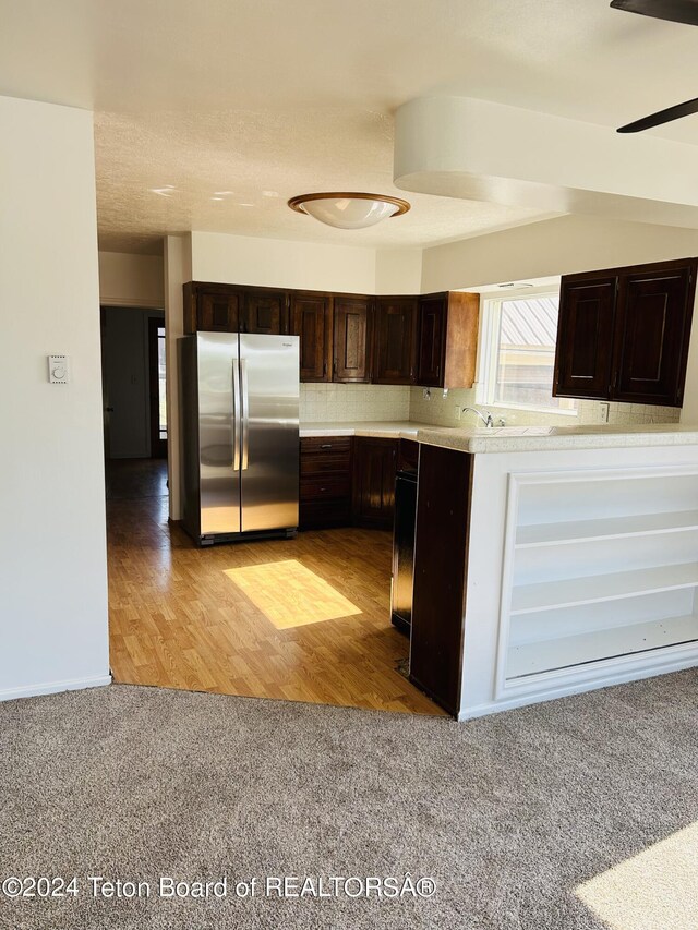 kitchen with stainless steel fridge, dark brown cabinets, backsplash, light wood-type flooring, and ceiling fan